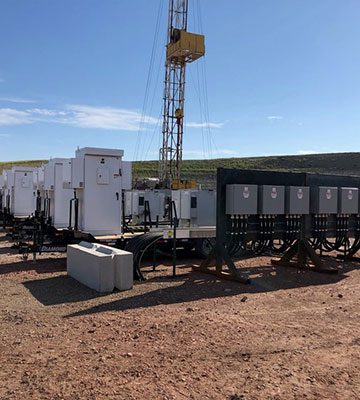 A group of trucks parked in the dirt near a drilling rig.