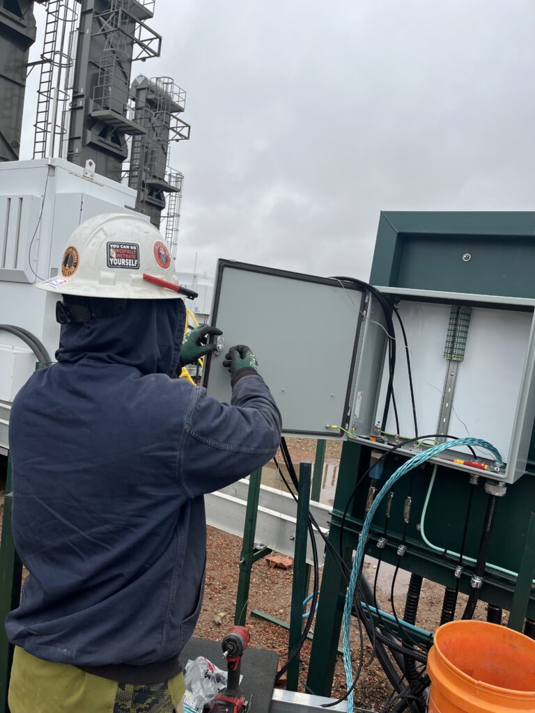 Automation technician gaining hands-on experience while working on a control panel at an oil and gas site