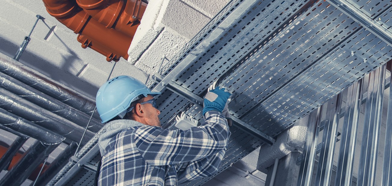 Electrician installing overhead cable tray for fiber and power routing in a processing plant